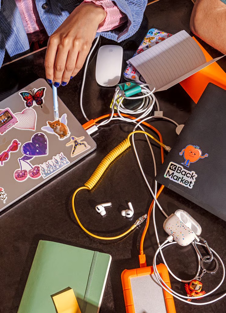 Overhead photo of a creative desk with laptops, accessories, and colorful stickers